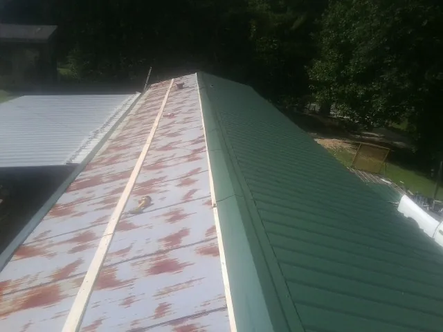 Old rusted panels beside newly installed green metal roofing — Wind Damage Roof Repair by Roofing Brothers in Eudora