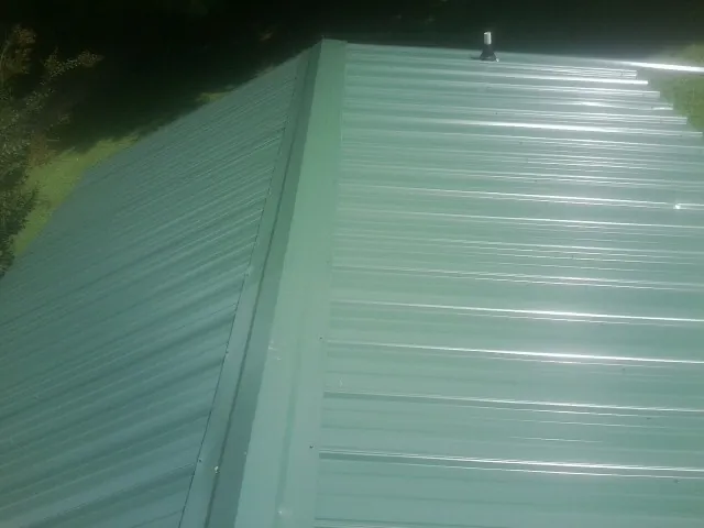 New green metal panels meeting at the ridge of a roof — Flat Roof Repair work by our crew in Eudora