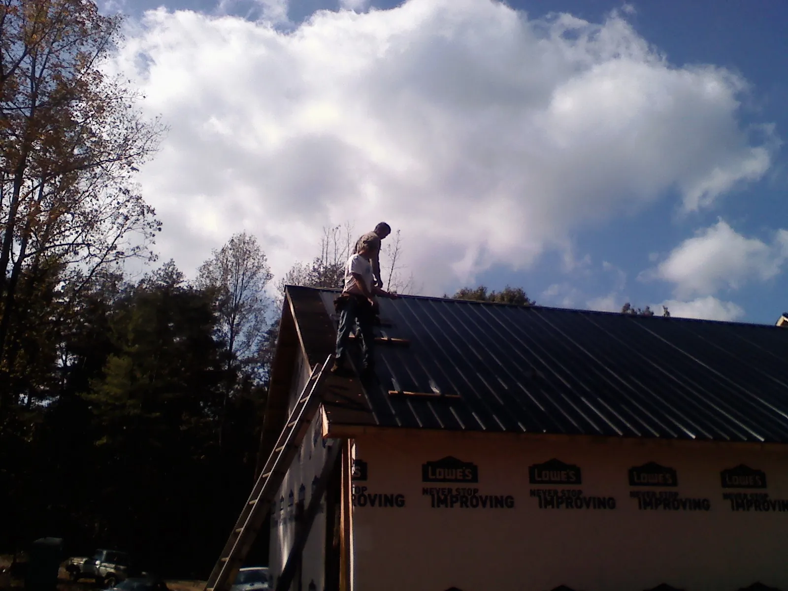 Roofer fastening dark metal panels high against a cloudy sky, from a Roof Inspection job in Eudora