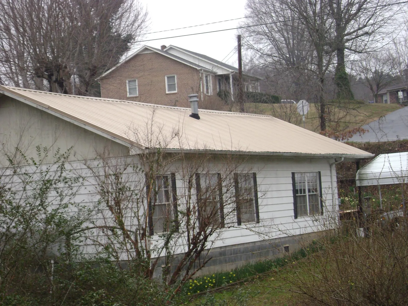 Tan metal roof on a white sided house set into a hillside — Commercial Roofing by Roofing Brothers in Eudora