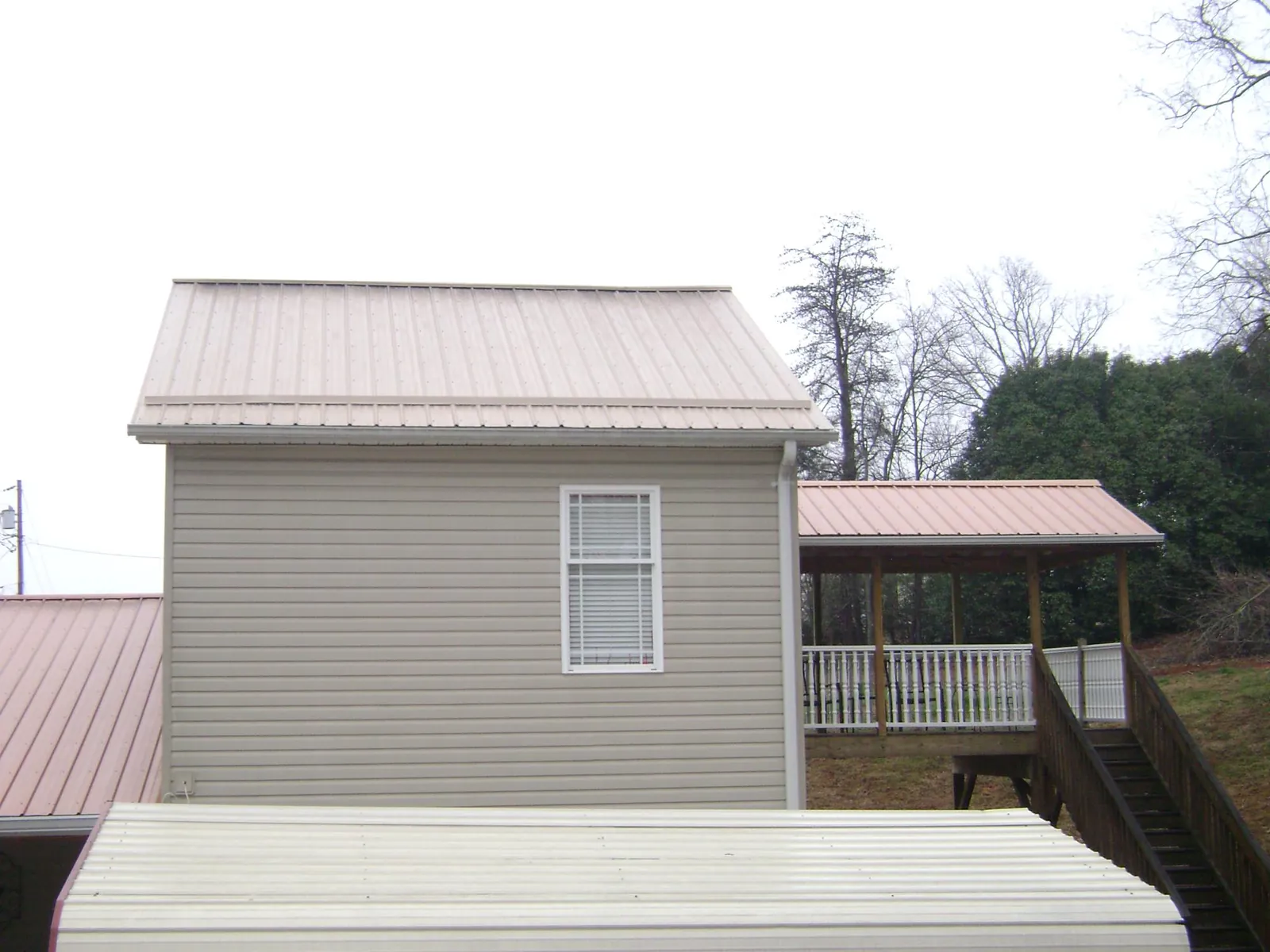 Tan metal roofs on a two story addition and attached porch, from a Roof Replacement job in Eudora